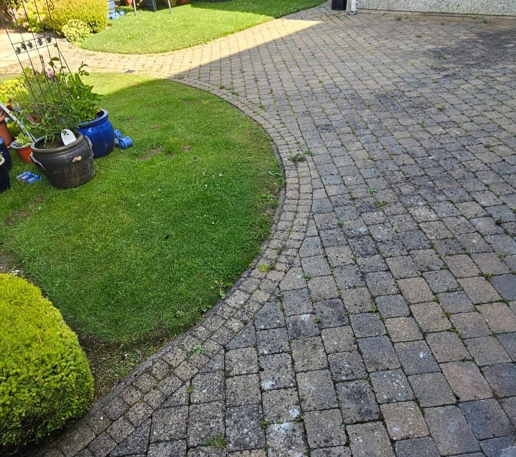 Curved block paving driveway before cleaning, grime and weeds dulling the surface